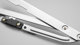 A retractable utility knife with a silver metal blade extended, placed on a light gray surface.